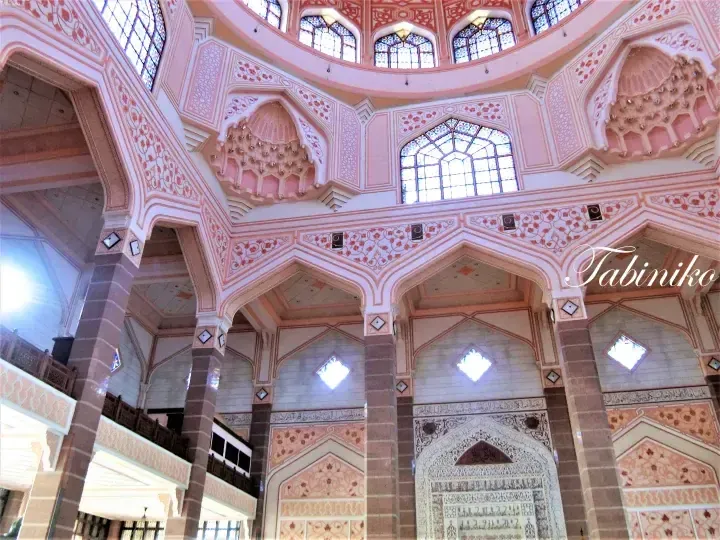 Pink interior of Putrajaya Mosque featuring intricate arches, stained glass windows, and detailed Islamic calligraphy.