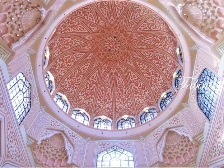 Ornate pink and white dome interior with intricate geometric patterns and stained glass windows at Putrajaya Mosque.