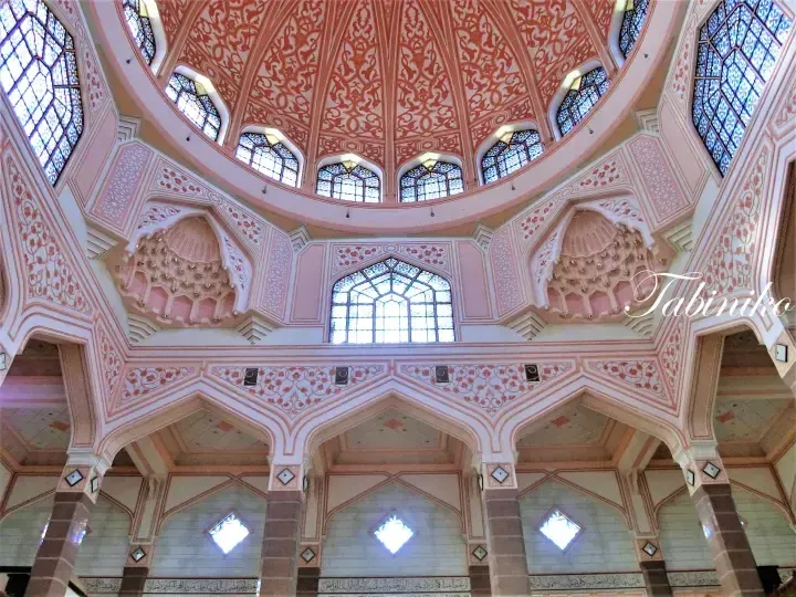 Ornate pink and white interior of Putrajaya Mosque featuring intricate stained glass windows and detailed ceiling patterns.
