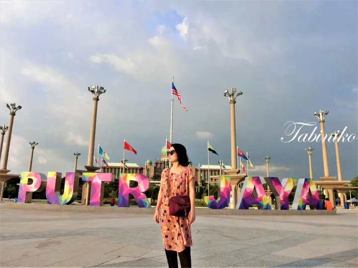 首相府を背景にカラフルな「PUTRAJAYA」の文字の前でポーズをとる女性。