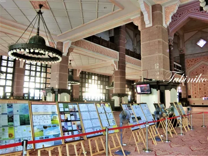 Interior of Putra Mosque with pink granite pillars, chandeliers, and informational displays about Islam.