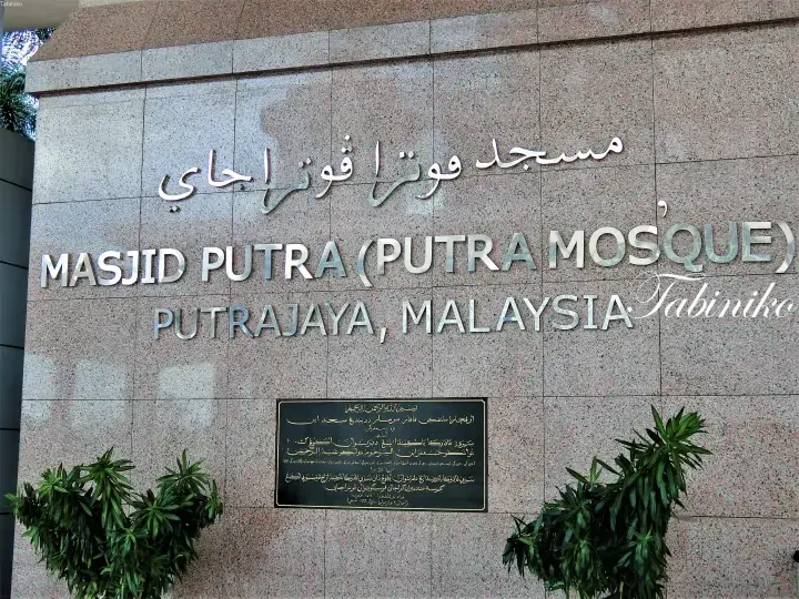 Signage for Masjid Putra (Putra Mosque) in Putrajaya, Malaysia, featuring Arabic and English text on a granite wall.