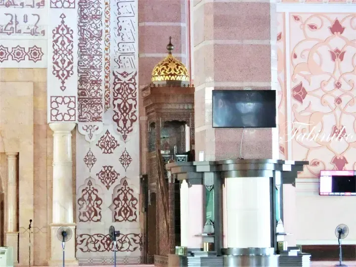 Interior view of a mosque featuring ornate Arabic calligraphy, a wooden minbar, and a golden dome.