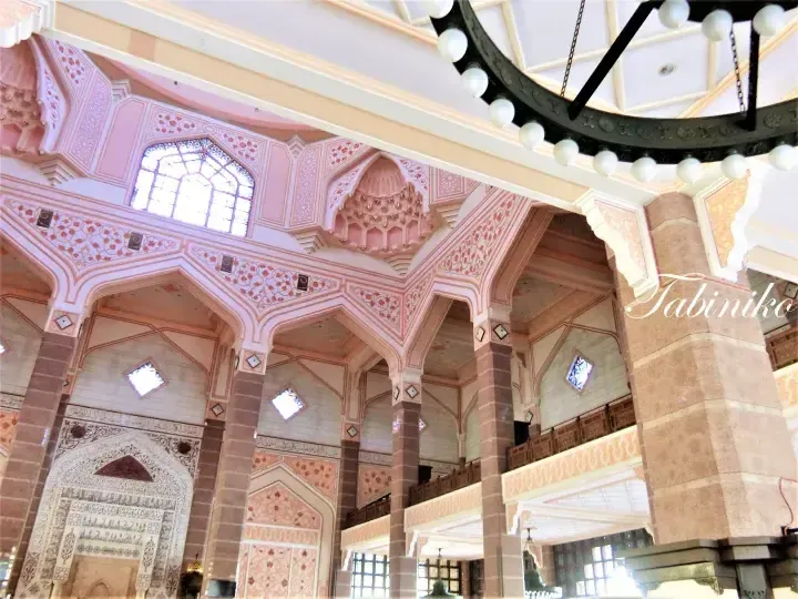Pink and cream Islamic architectural interior featuring ornate arches, stained glass windows, and a large chandelier.