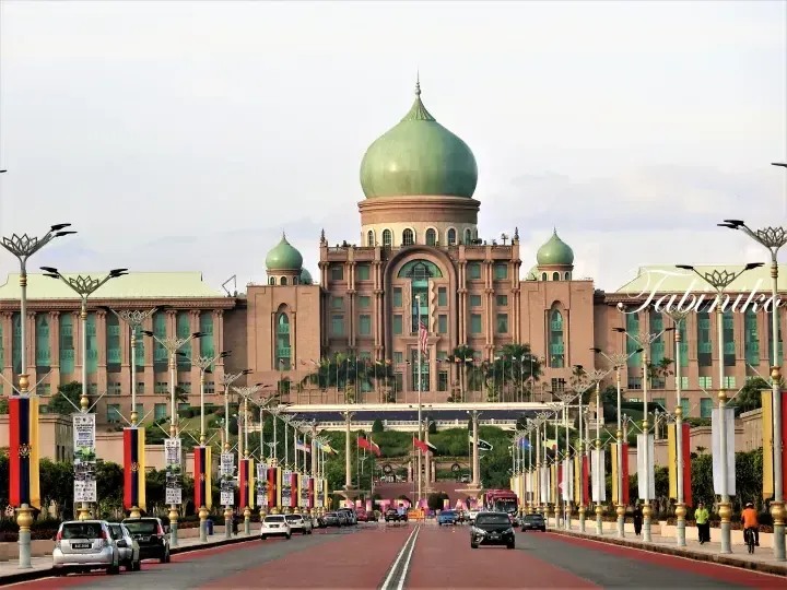 The majestic Putra Mosque with its green dome in Putrajaya, Malaysia, viewed from the wide boulevard lined with flags.