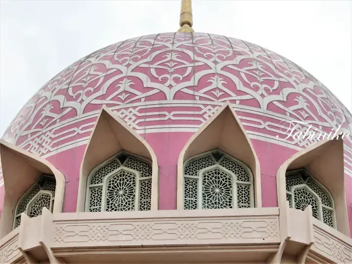 Pink dome with intricate white floral patterns and arched windows at Putra Mosque in Putrajaya