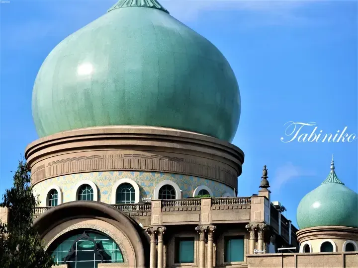 Close-up of the large green dome and ornate facade of a mosque against a blue sky.