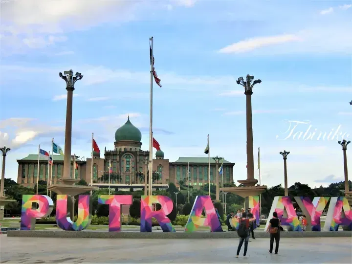 Colorful PUTRAJAYA letters in front of the Perdana Putra building with a green dome and Malaysian flags.