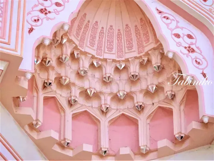 Ornate pink ceiling with intricate mirror work and floral patterns in a traditional Indian palace interior.