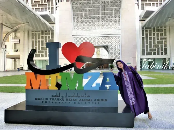 Woman in purple abaya posing with colorful I Love MITZA sign at Masjid Tuanku Mizan Zainal Abidin, Putrajaya