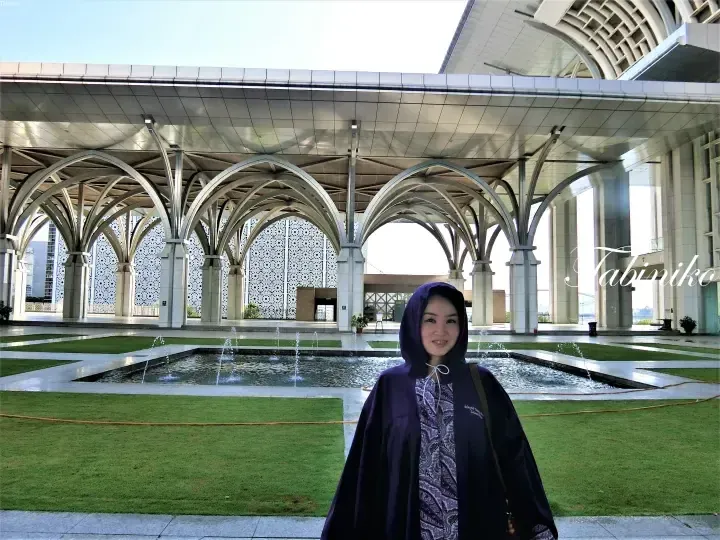 Woman in purple hijab smiling at Putra Mosque’s courtyard with distinctive arches and fountain.