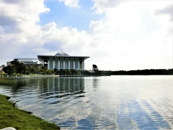 Federal Mosque Putra Mosque reflected in the lake at Putrajaya, Malaysia, under a cloudy blue sky.