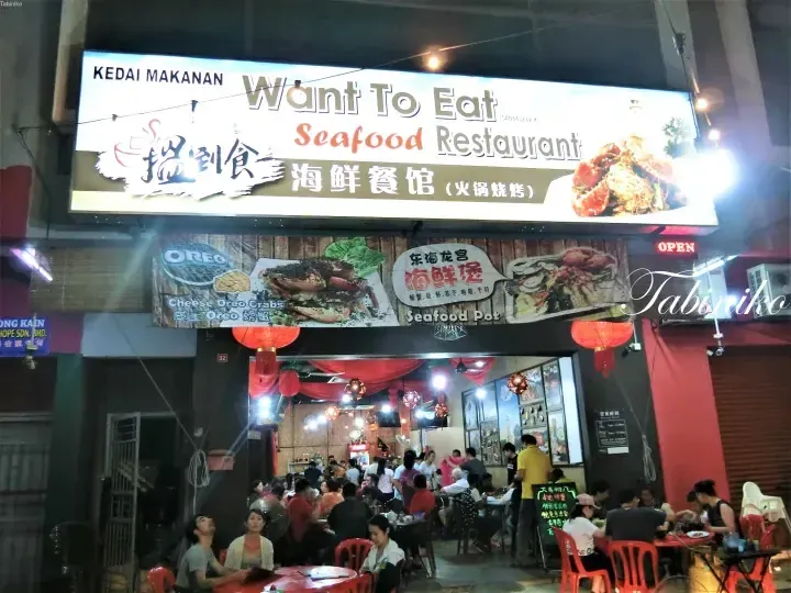 Want To Eat Seafood Restaurant storefront with illuminated sign, red lanterns, and patrons dining inside.