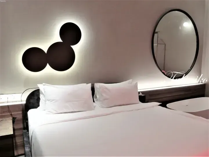 Modern hotel bedroom with a bed, circular mirror, and Mickey Mouse-shaped wall art.