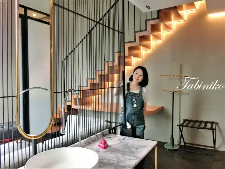 Woman in denim overalls stands by a modern staircase with integrated LED lighting in a stylish interior space.