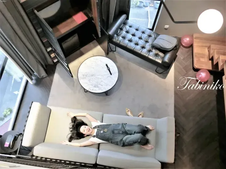 High-angle view of a woman relaxing on a sofa in a modern hotel suite with a marble coffee table and leather daybed.