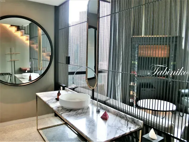 Modern bathroom vanity with marble countertop, round mirror, and black slatted room divider in a luxury hotel suite.
