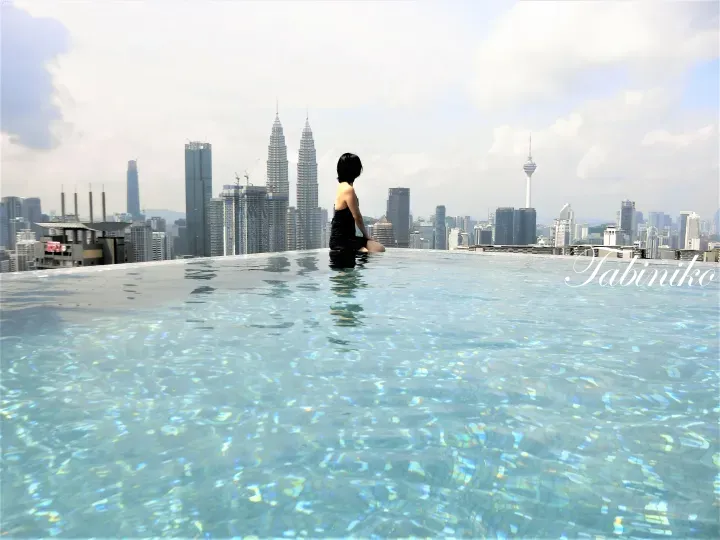 Woman sitting in rooftop infinity pool with Petronas Twin Towers and Kuala Lumpur skyline in background