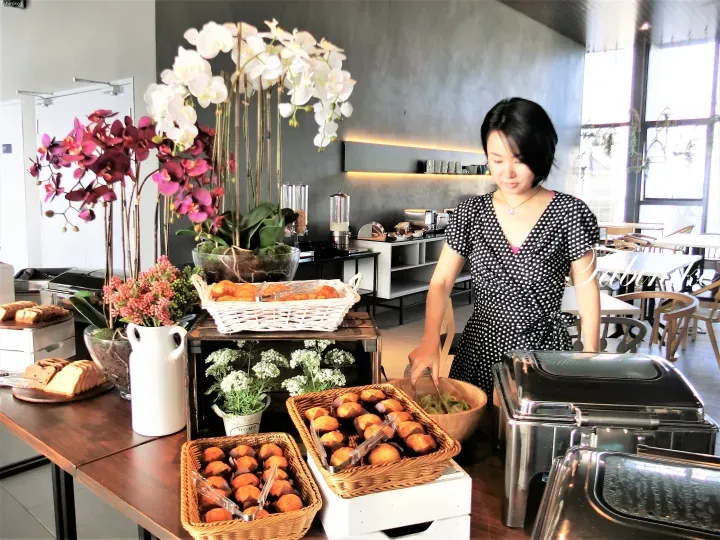 Woman in polka dot dress selecting food from a buffet table featuring orchids and pastries at a Malaysia property.
