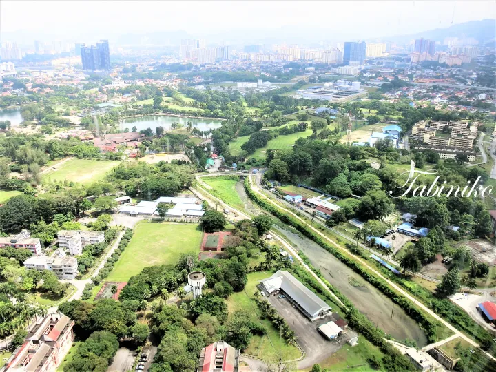 遠くに高層ビルが立ち並ぶ都市のスカイラインを望む、緑豊かな風景と川、湖、ゴルフコースの空中写真。
