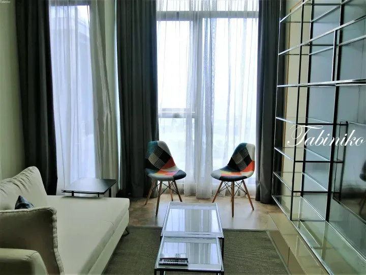 Modern living room with white sofa, colorful chairs, and glass shelving in a high-rise apartment