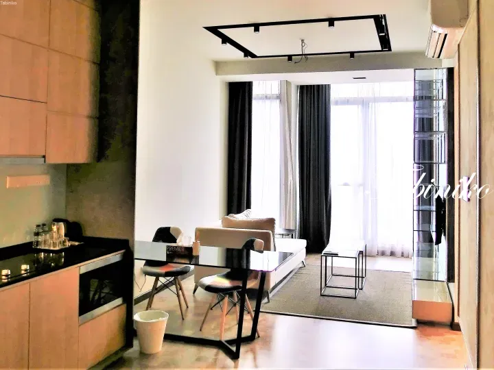 Modern apartment interior featuring a kitchen, dining table, and living area with large windows and city views.