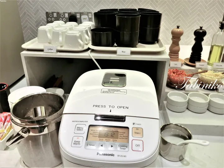 Panasonic rice cooker and coffee station with cups and bowls at a hotel breakfast buffet.