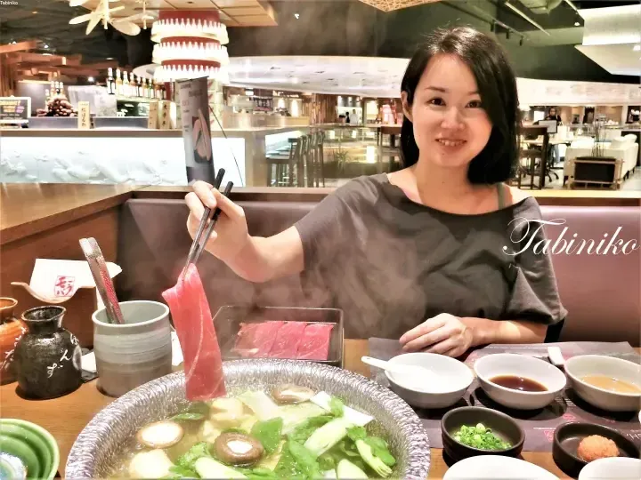野菜がたっぷり入った蒸し上がる鍋料理の前で、箸で生肉の薄切りを挟む女性。