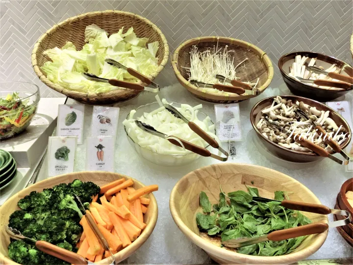 A variety of fresh vegetables like broccoli, carrots, cabbage, and mushrooms displayed in bowls at a buffet station.