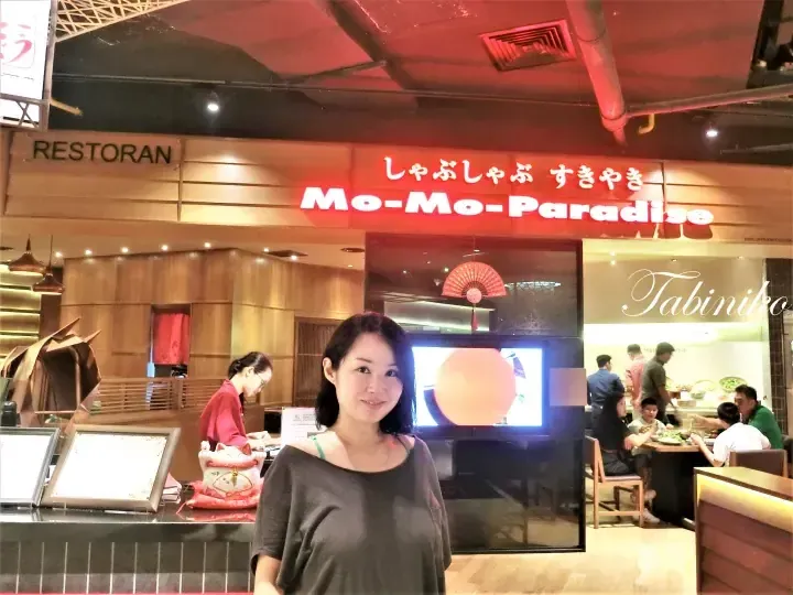 女性、モモパラダイスしゃぶしゃぶすき焼きレストランの入り口前で笑顔で立っている。
