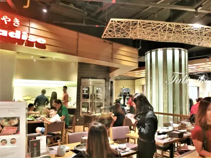 焼き肉パラダイス店内で食事をする客とオープンキッチンが見えるレストランの風景。