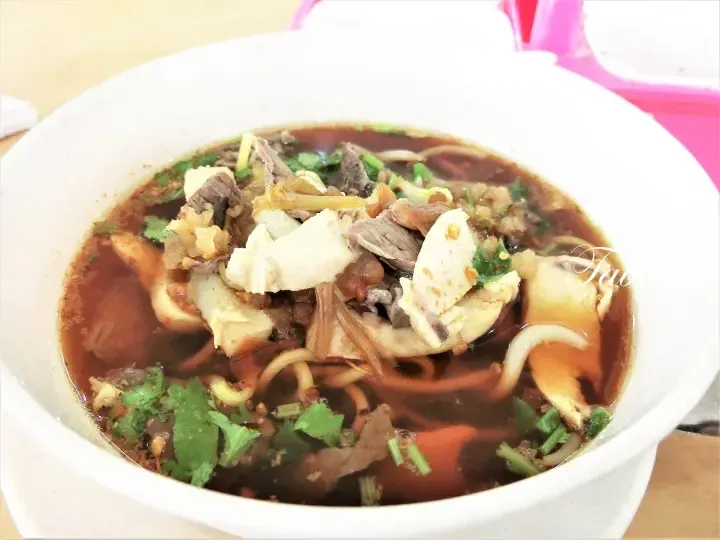 A bowl of rich beef noodle soup with tender meat slices, fresh herbs, and savory broth.