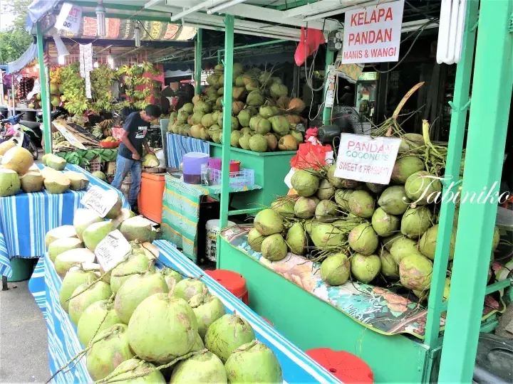Pandan coconuts displayed at a roadside stall with signs reading Kelapa Pandan Manis & Wangi