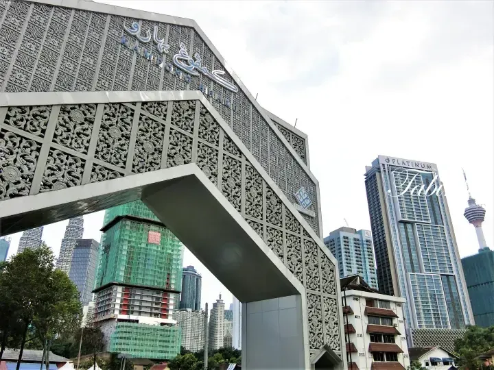 Kampung Bharu archway with intricate carvings, overlooking Kuala Lumpur skyline including Platinum Suites and KL Tower