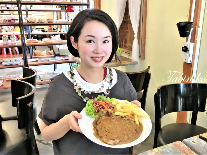 ステーキ、フライドポテト、サラダを盛り付けたお皿を手に笑顔を見せる女性。