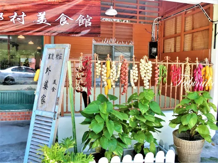 Wan Mao Village restaurant exterior with hanging dried vegetables and a wooden signboard.