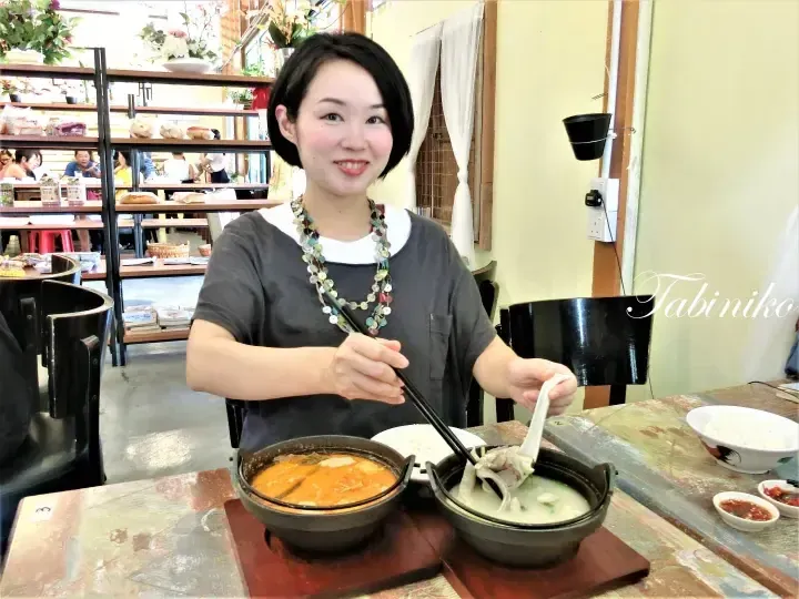A woman smiles while holding chopsticks over two bowls of soup at a restaurant table.