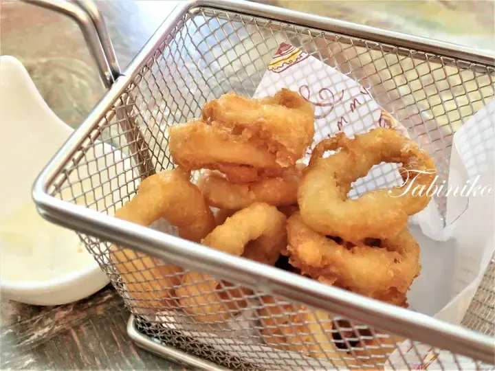 Golden fried calamari rings served in a wire basket with a side of creamy dipping sauce.