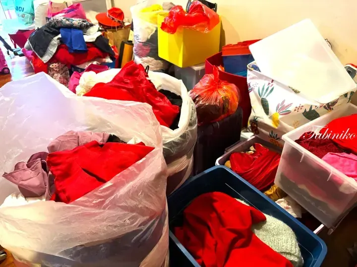 A room filled with large plastic bags and storage containers packed with red clothing and other items.