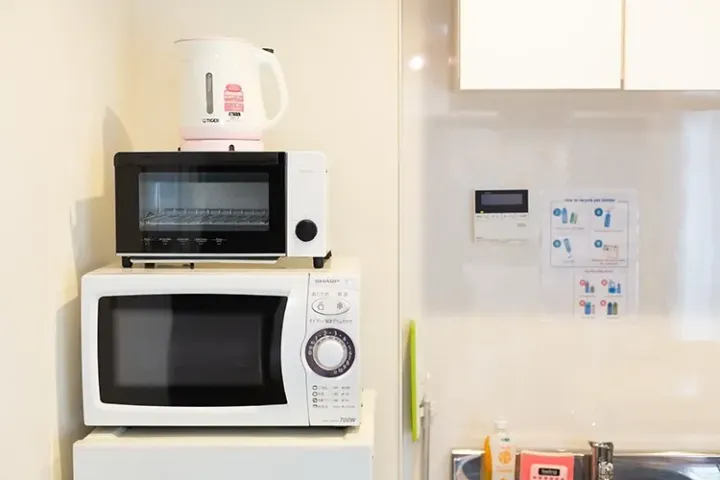 Stacked kitchen appliances including a white microwave, toaster oven, and electric kettle in a modern rental unit.