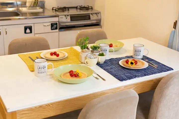 A bright dining table set with yellow and blue placemats, mugs, and plates of food in a modern kitchen.