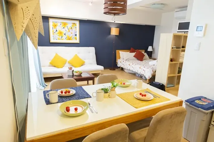 Bright studio apartment featuring a dining table set for breakfast, a white sofa, and a bed in the background.