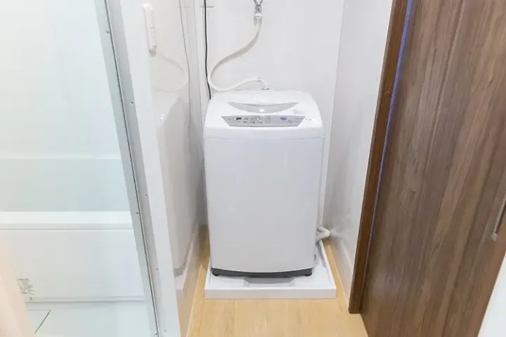 White top-loading washing machine installed in a compact laundry space next to a bathroom door.