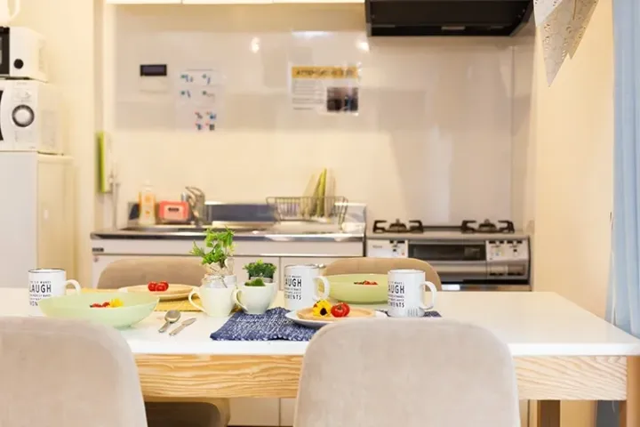 Modern kitchen with a dining table set for breakfast, featuring white mugs and fresh fruit in a bright apartment.