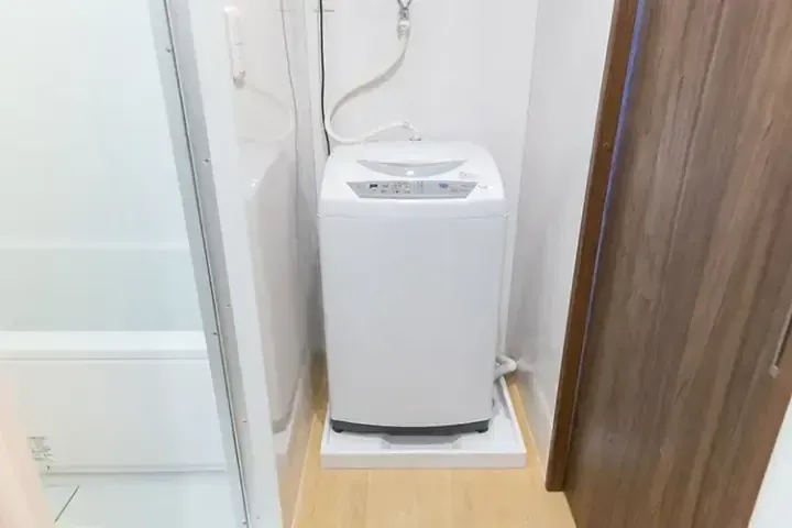 浴室のドアの隣に設置された、コンパクトな洗濯スペースの白い縦型洗濯機。