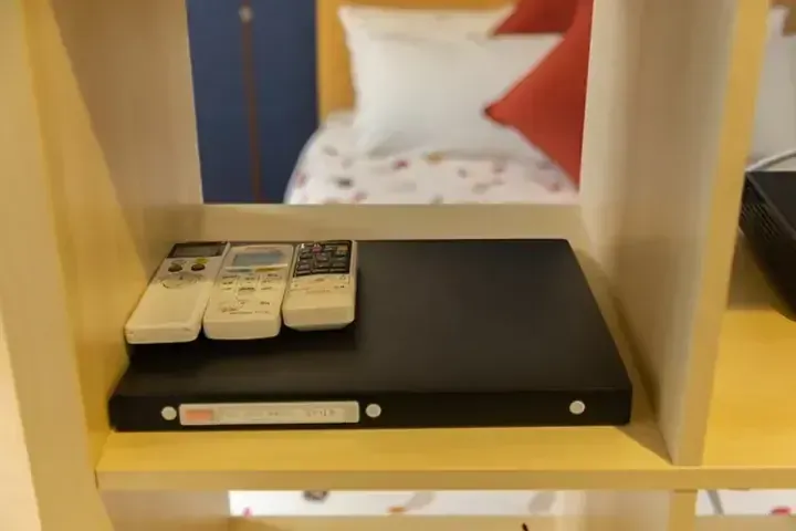 ホテルの部屋の木製棚に置かれた、黒いファイルと3つのリモコン。