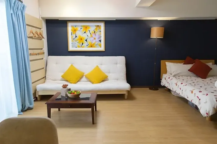 Cozy studio apartment with a white sofa, yellow cushions, and a floral painting on a navy blue wall.