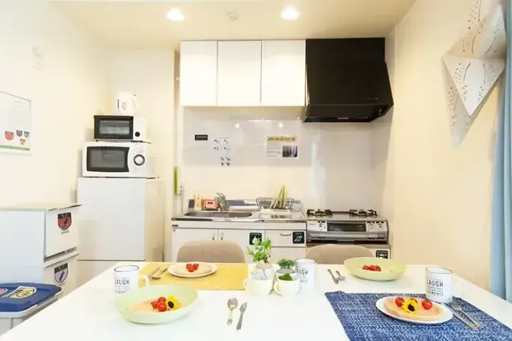 白いキャビネットと黒いレンジフードを備えたモダンなキッチンと、カラフルな朝食が並んだダイニングテーブル。