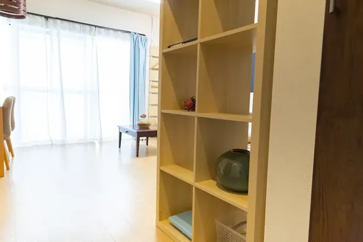 Light-filled living room with a wooden shelving unit, blue curtains, and a coffee table near large windows.