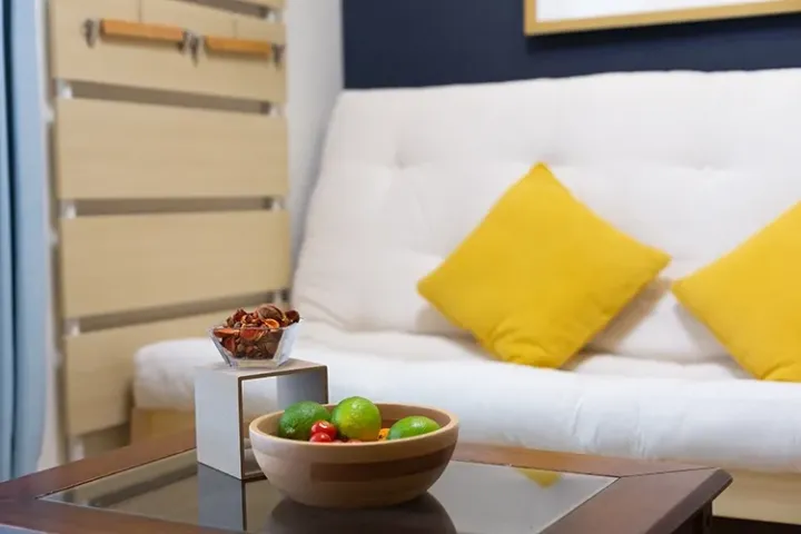 Modern living room with white sofa, yellow cushions, and coffee table displaying fresh limes and dried snacks.